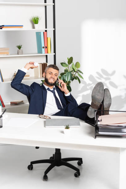 istock Angry businessman holding clumped paper while talking on smartphone in office 1284296920