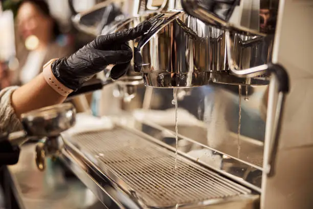 Close up photo water drops falling on a drip tray of an espresso machine while barista pushing the button