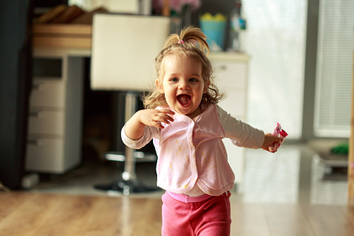 Three quarter length shot of jolly little baby girl running towards someone behind a camera and smiling with excitement.