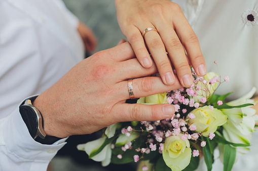 Close-up mid section of a newlywed couple with wedding rings and bouquet