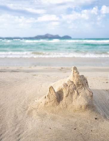 primer plano de un castillo de arena destruido por las olas en una playa con el mar azul en el fondo en un día soleado y nublado, vertical photo