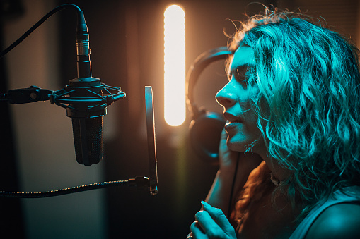 One woman, beautiful female vocalist wearing headphones and singing into microphone in recording studio.