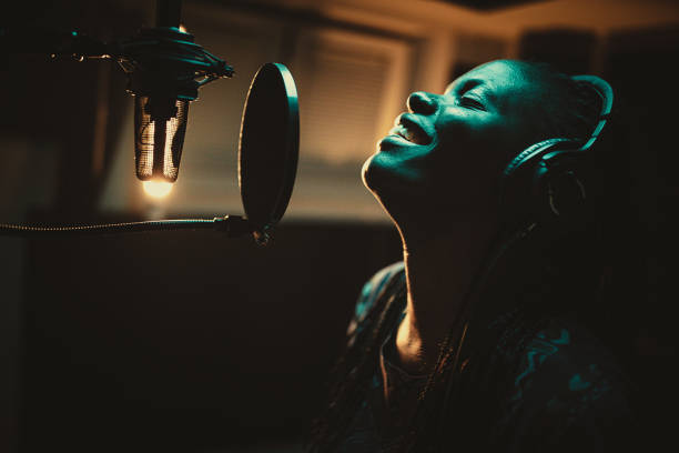 Young African-american female singer recording song in the music studio One beautiful young African-american female singer recording album in the professional music studio. Female vocalist wearing headphones and singing into microphone in recording studio. artist stock pictures, royalty-free photos & images