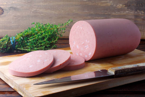 piece of whole raw pork bologna on cutting board with some slices. stock photo