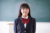 日本の中学生の女の子が笑顔で教室に立っています