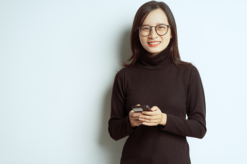 Portrait of a smiling asian businesswoman standing with crossed arms and wearing glasses, holding smartphone