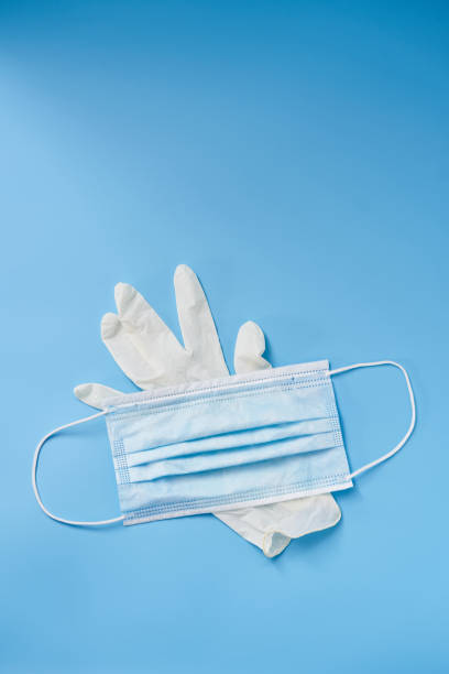 istock Isolated glove and face mask on a blue background. Protection during Covid-19 quarantine 1284352445