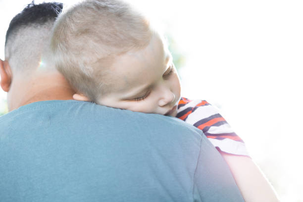 istock A young child is sleeping in his father's safe and protective embrace while on walk. Portrait of cute adorable blond caucasian toddler boy sleeping on fathers shoulder. Single father concept. 1284359134
