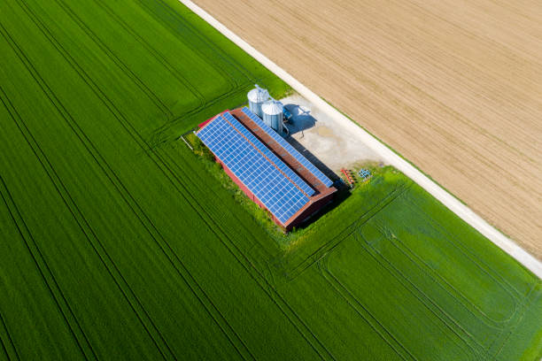 Agricultural building with solar panels and silos between green fields, viewed from above.