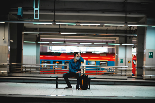 Young Caucasian man wearing protective face mask checking his smartphone while is waiting for the train