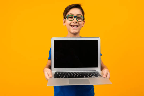 istock joyful caucasian boy shows laptop screen with mockup on yellow studio background with copy space 1284368333