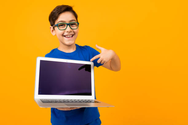 istock joyful caucasian boy holds laptop screen forward with mock up on yellow studio background with copy space 1284368338