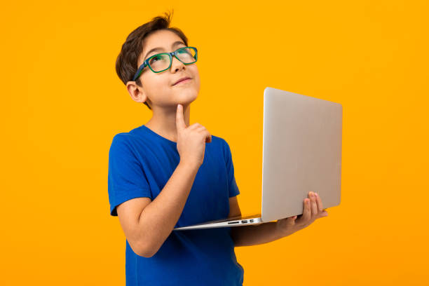 istock smart boy in a blue t-shirt thinking holding a laptop in his hands on a yellow studio background 1284368343