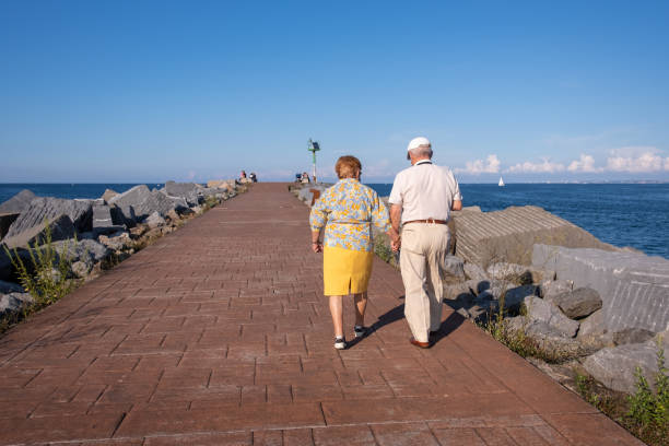 海のそばを歩く先輩夫婦。健康的なライフスタイルを持つ高齢者。手をつないで長持ちするカップル。スペインの平均余命は高いです。スペイン北部 エウスカディ バスク 州 - holding hands couple senior couple togetherness ストックフォトと画像