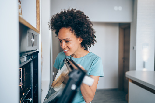 istock Young woman opening oven to check food. 1284369958