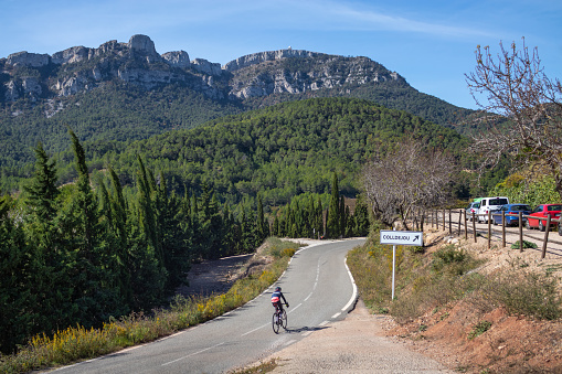 Spain; Oct 2020: Person riding a bicycle on a road in the middle of the mountains. Leisure with sunny weather on the weekend. Tarragona, Serra de Llaberia, Catalonia, Spain