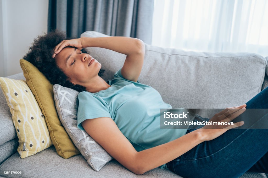 Woman with high fever at home. Sick young woman lying on the couch and holding her head with hand. Ill woman lying on the sofa with high temperature. Tired Stock Photo