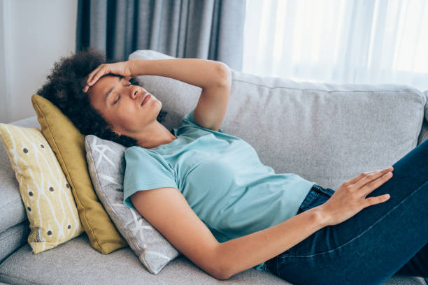Woman with high fever at home. Sick young woman lying on the couch and holding her head with hand. Ill woman lying on the sofa with high temperature. anemia stock pictures, royalty-free photos & images
