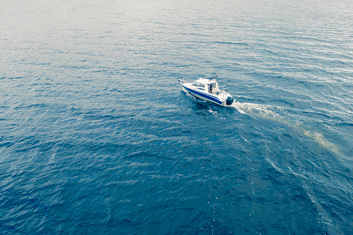 Aerial view fisherman on boat at the ocean. Top view beautiful seascape with the fishing boat. Aerial view fishing motor boat with angler. Ocean sea water wave reflections. Motor boat in the ocean.