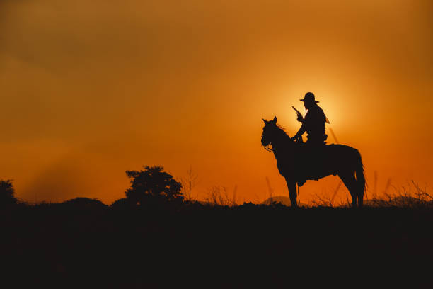 sylwetka kowboja jadącego na górze z żółtym niebem. - cowboy horseback riding nature blue zdjęcia i obrazy z banku zdjęć