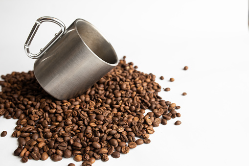 Coffee beans with an aluminum camp style mug on a white background.