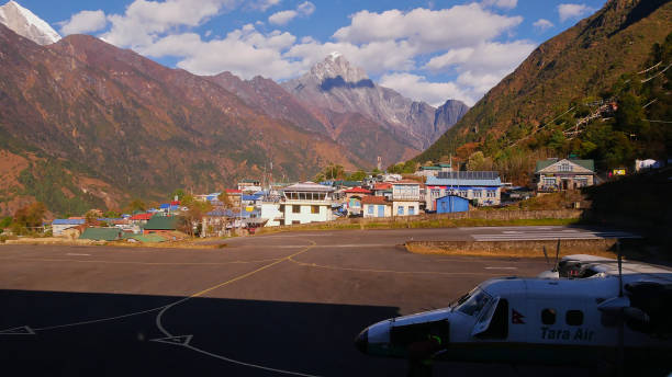 Tara Air plane ready for boarding in front of Tenzing-Hillary Airport terminal with runway, Sherpa village and Himalayan mountain range. stock photo