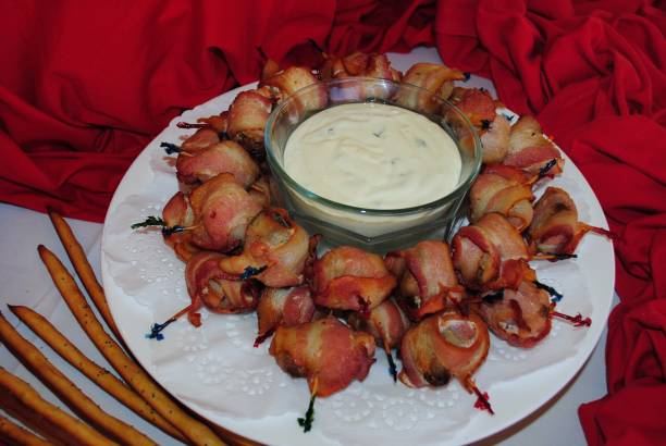 Round plate of rolled bacon appetizers with white sauce for dipping