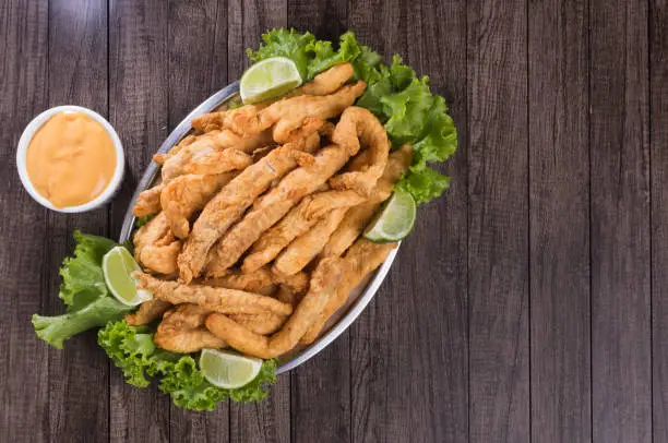 Photo of Breaded fried fish served on lettuce leaves with lemons and tartar sauce to accompany. Top gastronomic photography with space for texts on the right.