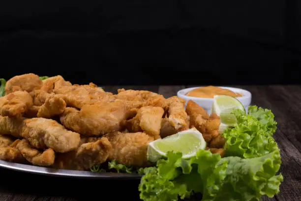 Photo of Portion and fried fish served on lettuce leaves with lemons and sauce to accompany. Gourmet gastronomic photography. Close-up photography.