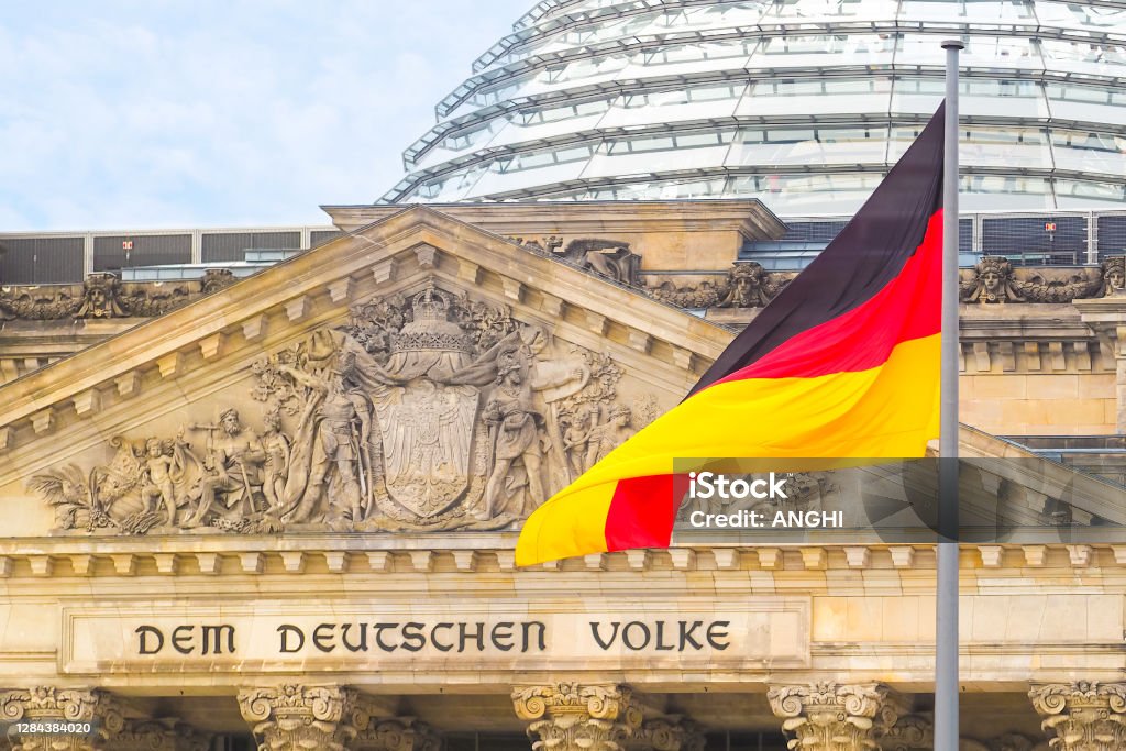 German flag on a background Reichstag building. The seat of the German Parliament or Bundestag, Berlin Mitte district. Inscription in German: To the German People Bundestag Stock Photo