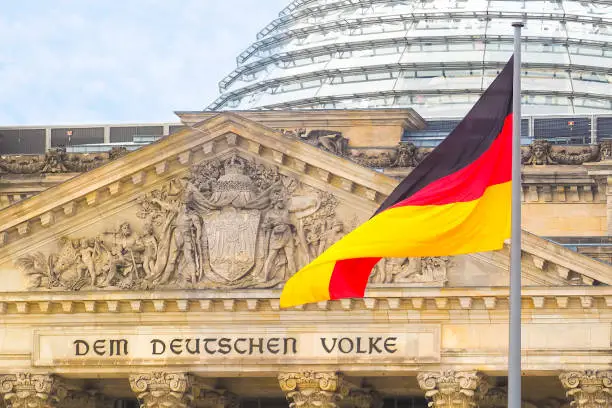German flag on a background Reichstag building. The seat of the German Parliament or Bundestag, Berlin Mitte district. Inscription in German: To the German People