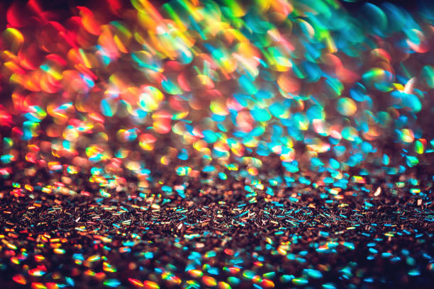 Multicolor blurred neon lights star flares and rainbow glitter on dark background. Bokeh lens flare glow. Festive backdrop with selective focus. Christmas New Year fireworks