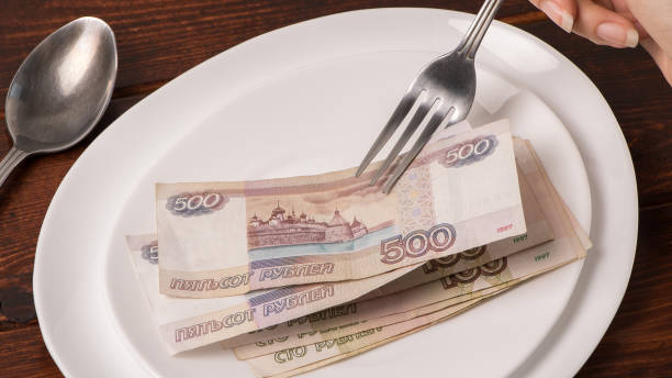 istock Russian rubles on a white plate. Keep money on the fork. Minimum subsistence level, food basket, minimum wage. Concept. Eat money, living wage. Economy. Crisis, inflation, business, Finance 1284394278