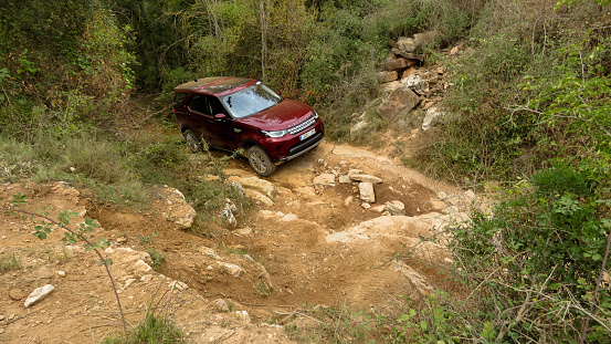 a Land Rover New Discovery, Discovery V, doing off road, 4x4, maroon, new, stock, seen from above going up a broken dirt road full of large stones