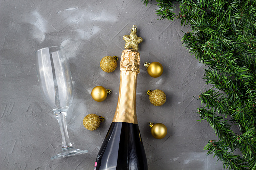 Two champagne glasses with gold balls and golden champagne bottle, green fir tree on grey background, copy space. Festive flat lay composition for Christmas or New Year.
