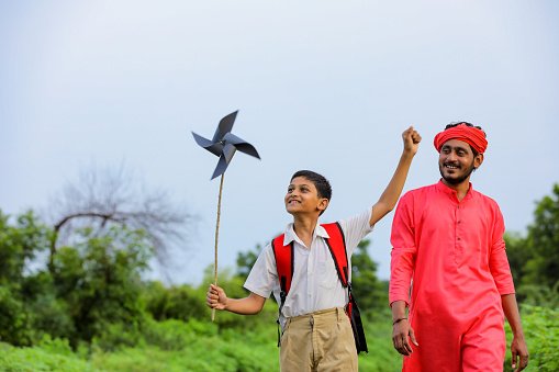 Indian farmer and his child playing with pinwheel on road side after school