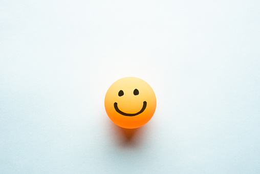 Happy smiley emoticon on a yellow ping pong ball with space for text blue background
