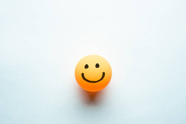 Happy smiley emoticon on a yellow ping pong ball with space for text blue background stock photo