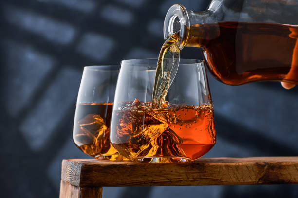 Two glasses of whiskey with ice on the counter, the glass is filled with whiskey from the bottle. Two glasses of whiskey with ice on the counter, the glass is filled with whiskey from the bottle. Two glasses of brandy on a tray on a blue background, the glass is filled with brandy from the bottle. cognac brandy stock pictures, royalty-free photos & images