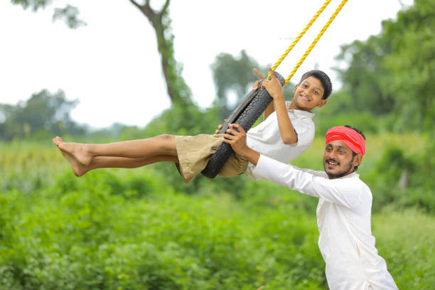 cute indian child playing with his father on swing made by tire and rope on tree at green field - freedom tire swing tire swing imagens e fotografias de stock