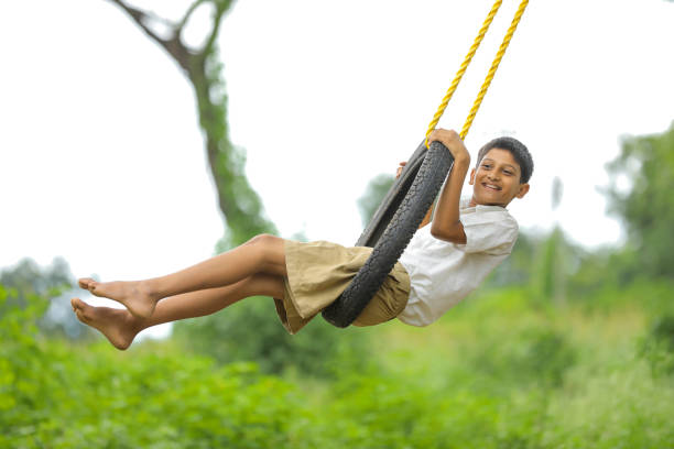 carino bambino indiano che gioca sull'altalena fatta da pneumatico e corda sull'albero sul campo verde - freedom tire swing tire swing foto e immagini stock