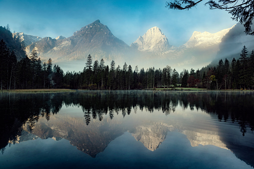 Foggy mountain landscape at dawn. Sunbeams in a valley. Lake and forest in a mountain valley at dawn. Natural panoramic landscape. Reflections on the surface of the lake. Banff National Park, Alberta, Canada.