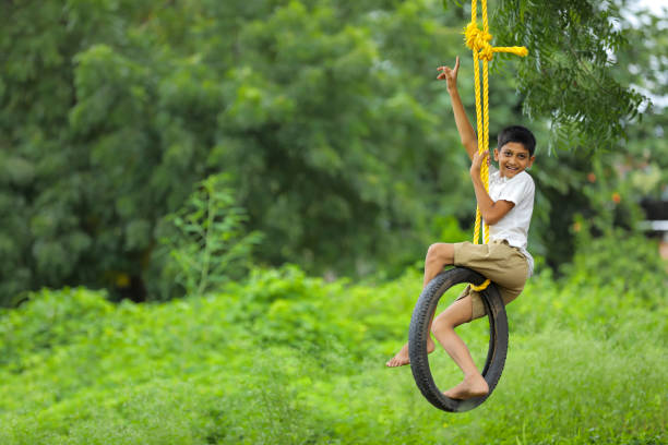 carino bambino indiano che gioca sull'altalena fatta da pneumatico e corda sull'albero sul campo verde - freedom tire swing tire swing foto e immagini stock