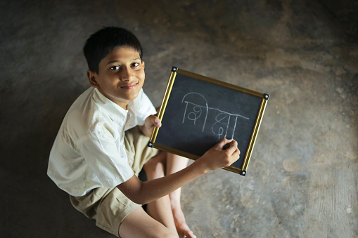 Cute indian child studying at home, writing shiksha word in Marathi language on Slate board