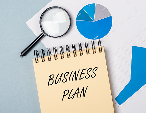 text Business Plan on yellow notebook on office table close up with analytical documents, strategy concept, banner