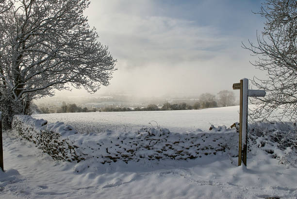 A snow covered field with old gate and distant hazy sunshine in winter