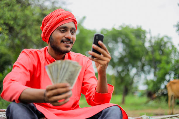 giovane agricoltore indiano che mostra soldi e parla al cellulare a casa - india indian culture business technology foto e immagini stock