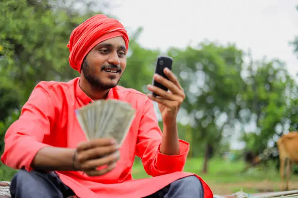 Young indian farmer showing money and talking on mobile phone at home