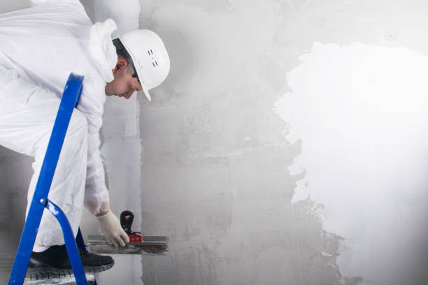 istock a master in a protective uniform and a white helmet, closes a crack in the wall with a white mixture, standing on a stepladder, there is a place for the inscription 1284411075