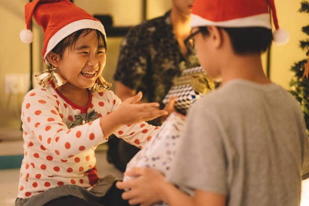 cute little asian chinese girl exchanging presents with her brother during christmas celebration - 6 12 months imagens e fotografias de stock